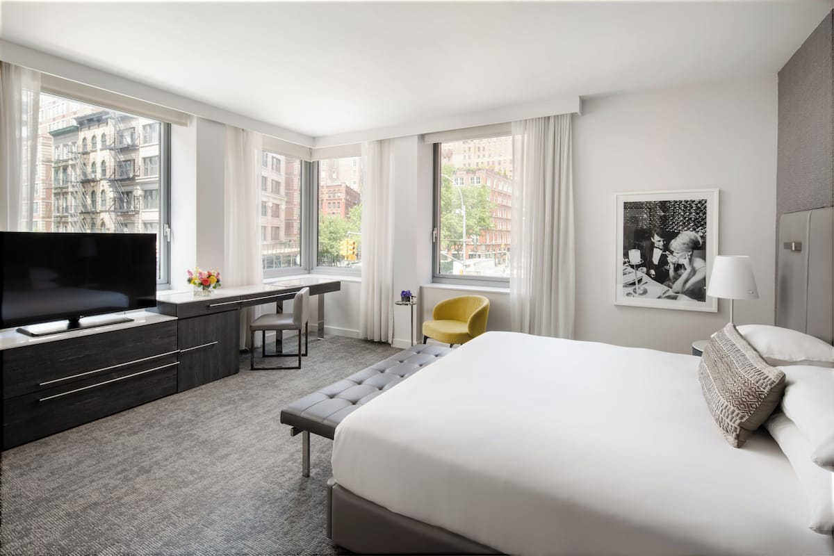 A modern hotel room with a large bed, a desk, a television, and a view of the cityscape.