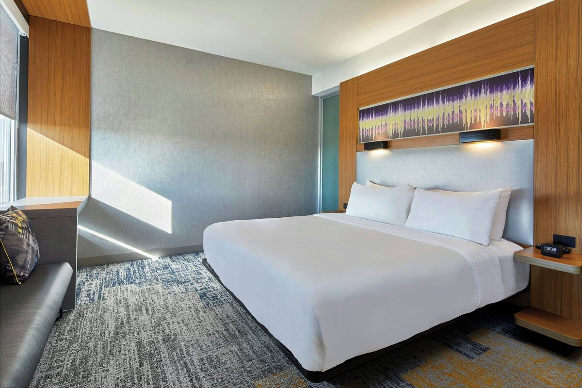 A modern hotel room with a large bed, a seating area, and a wall-mounted artwork.