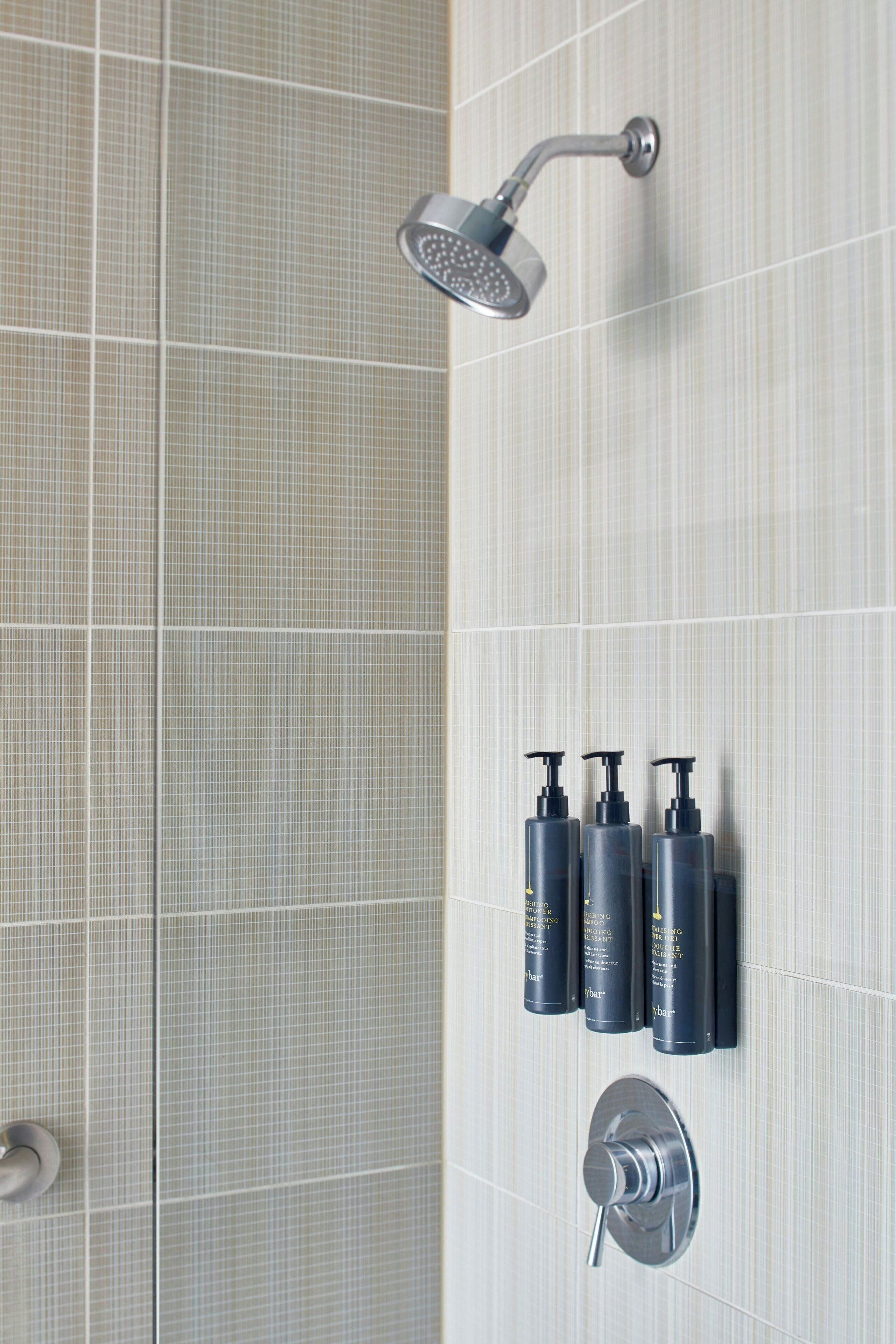 A bathroom with a shower, three bottles of shampoo, and a toilet.