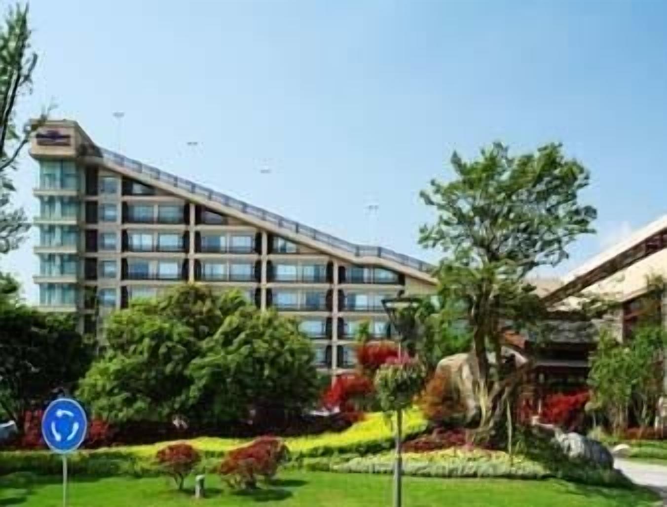 Een modern hotel met een meerlaags gebouw, een aangelegde tuin en een heldere lucht.