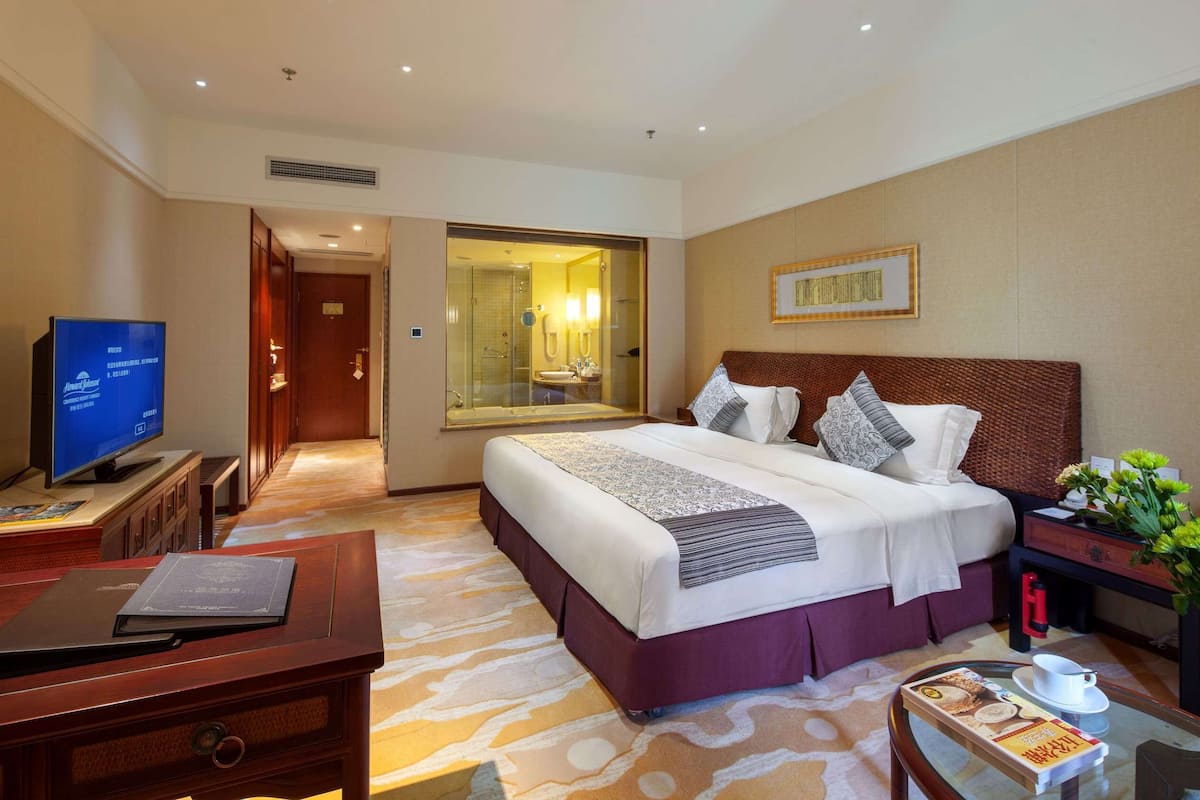 A hotel room with a large bed, a television, a desk with a laptop, and a bathroom visible through an open door.