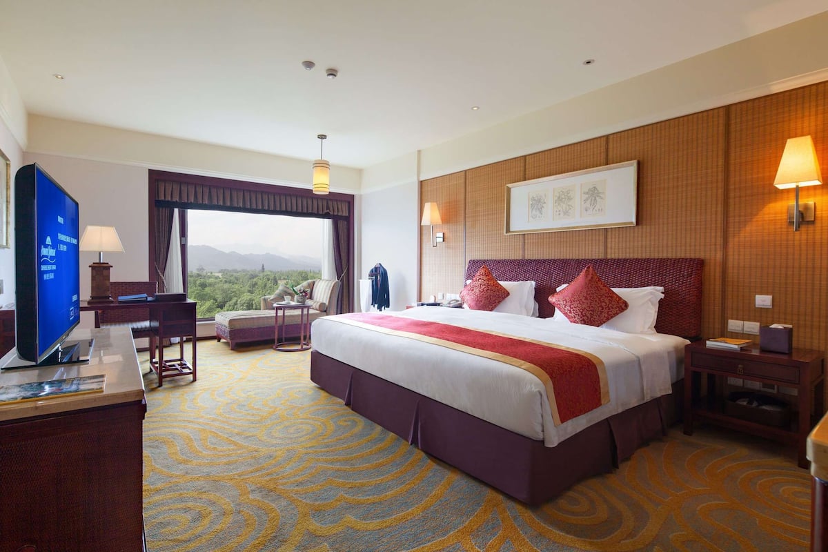 A hotel room with a large bed, a desk with a computer, a TV, and a view of the mountains.