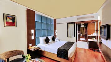 Una habitación de hotel con una cama grande, un televisor, un escritorio con una silla y una mesita con un jarrón de flores.