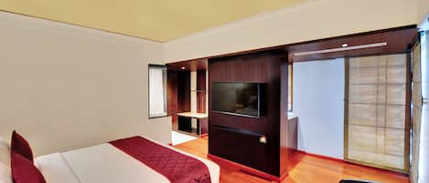 A hotel room with a bed, a TV, a seating area, and a sliding door leading to a balcony.
