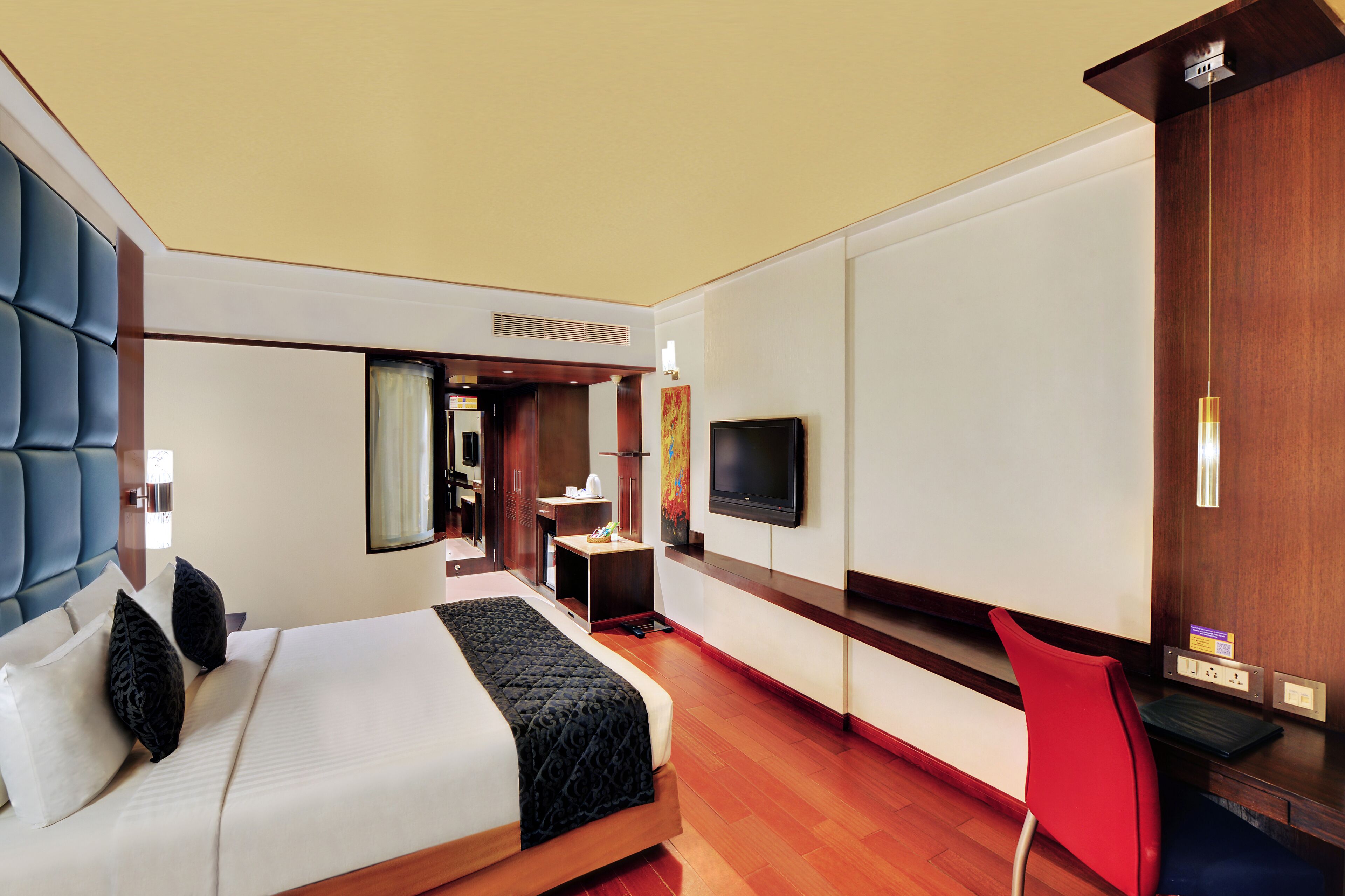 Habitación de hotel con una cama grande, un televisor en la pared, un escritorio con una silla y suelo de madera.