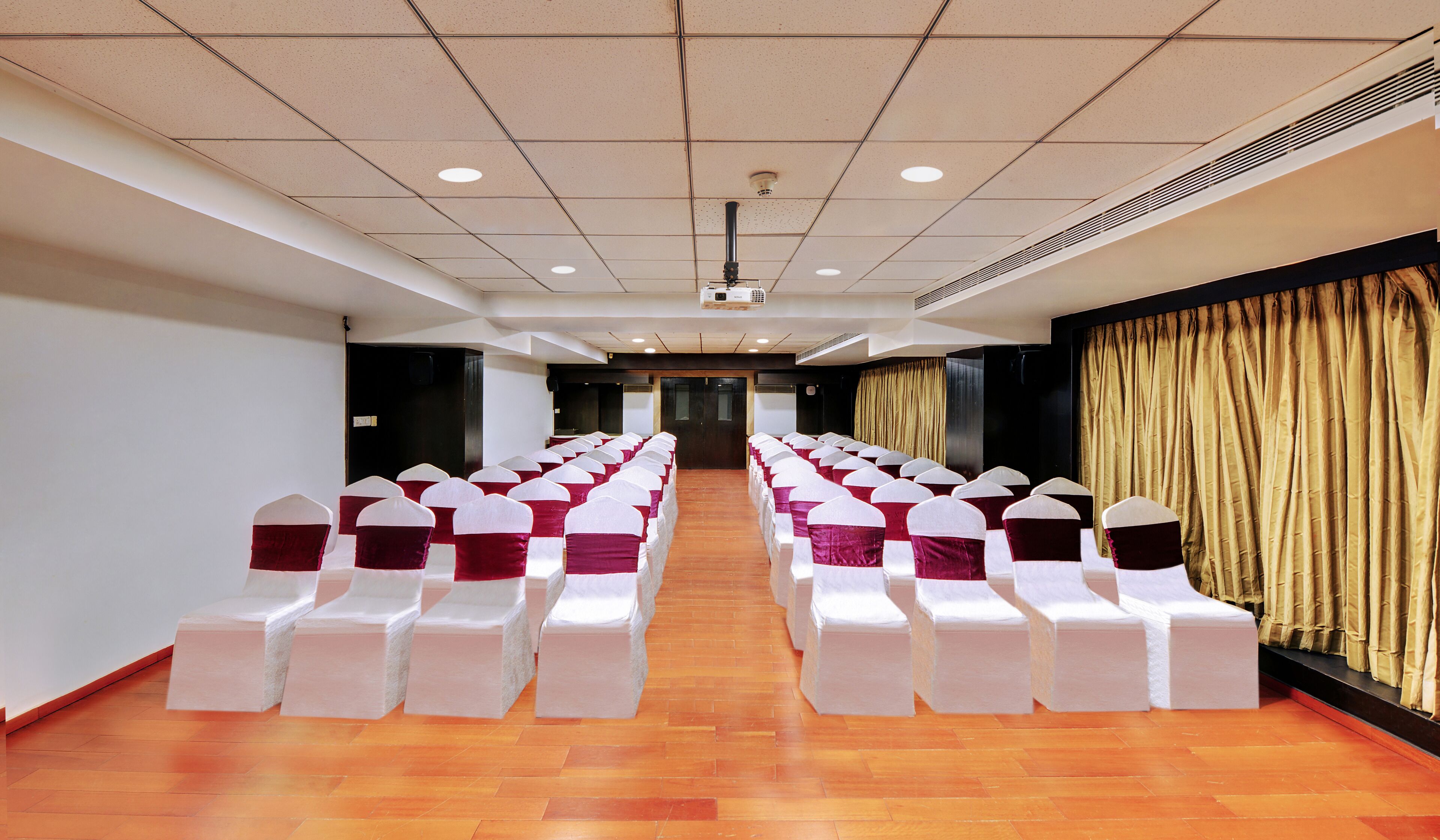 A conference room with rows of white chairs, a wooden floor, and a stage at the front.