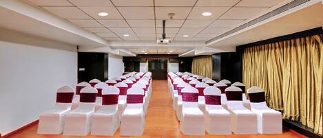 A conference room with rows of white chairs, a wooden floor, and a stage at the front.