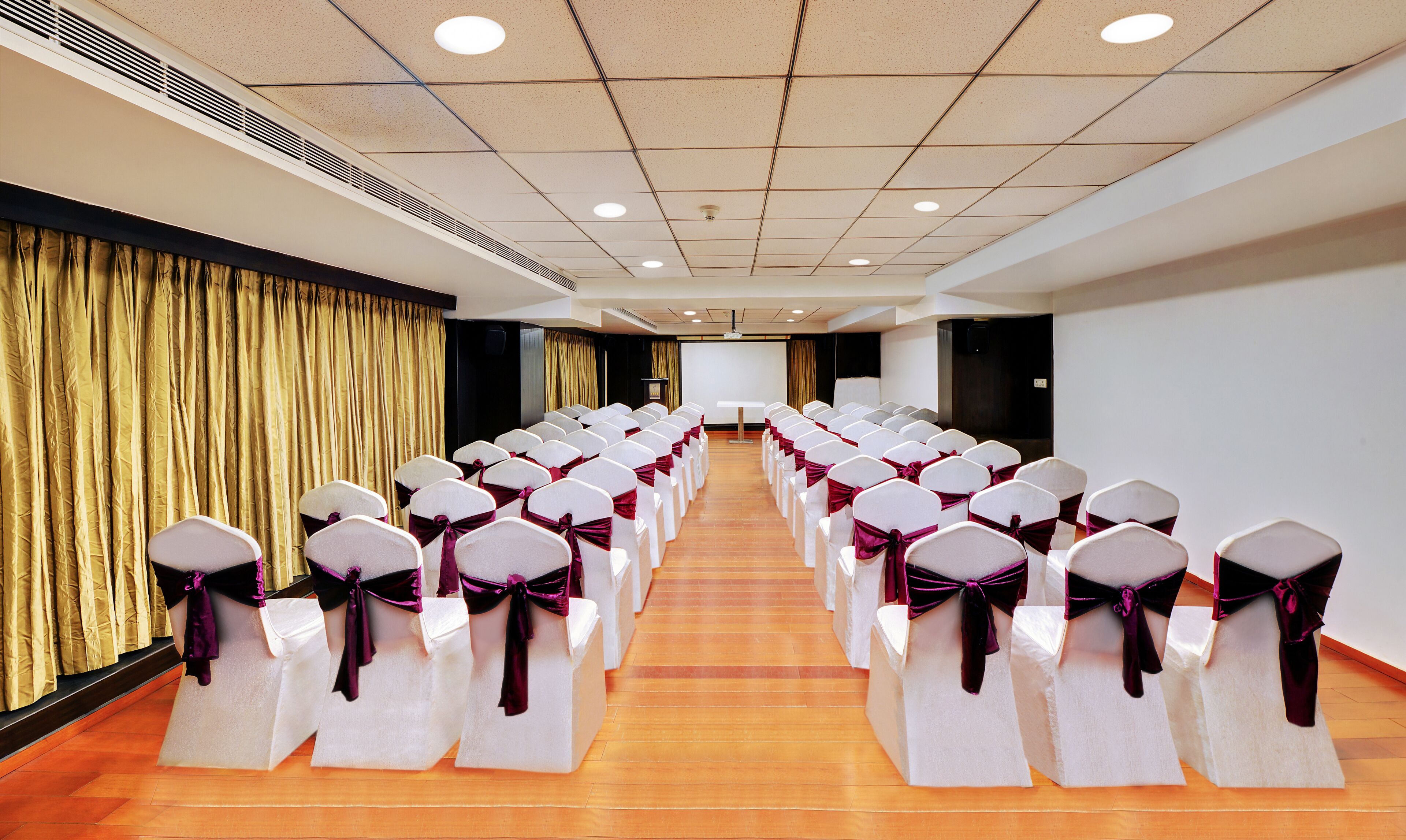 A conference room with rows of white chairs with purple sashes, a projector screen, and a stage.