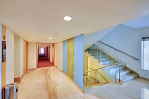 A modern hotel interior with a marble-floored hallway, a glass staircase, and a red carpeted corridor.