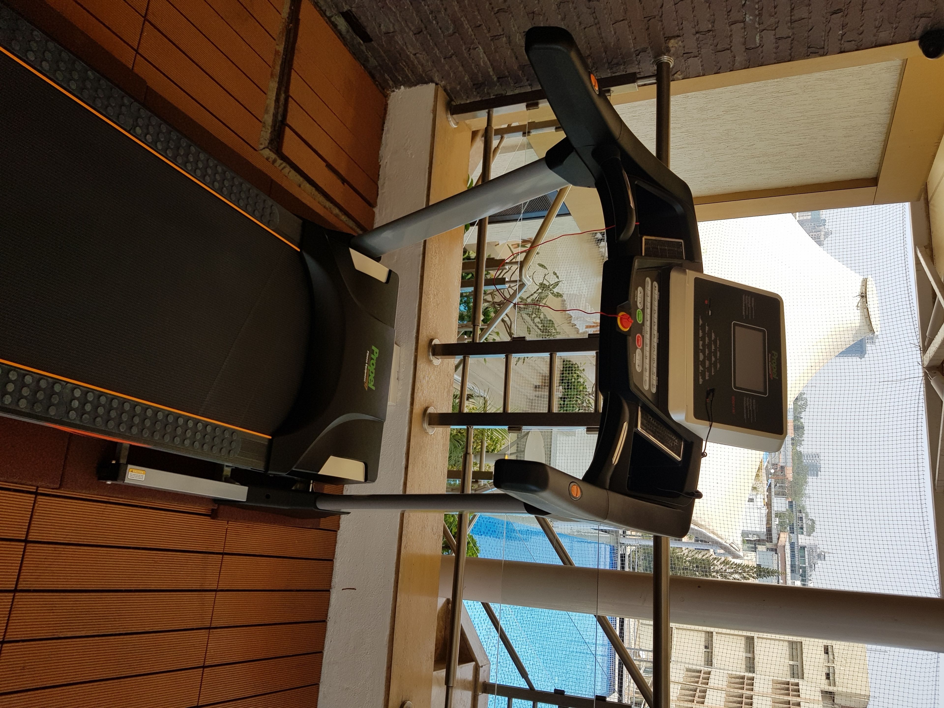 A treadmill in a room with a wooden floor and a window overlooking a building.