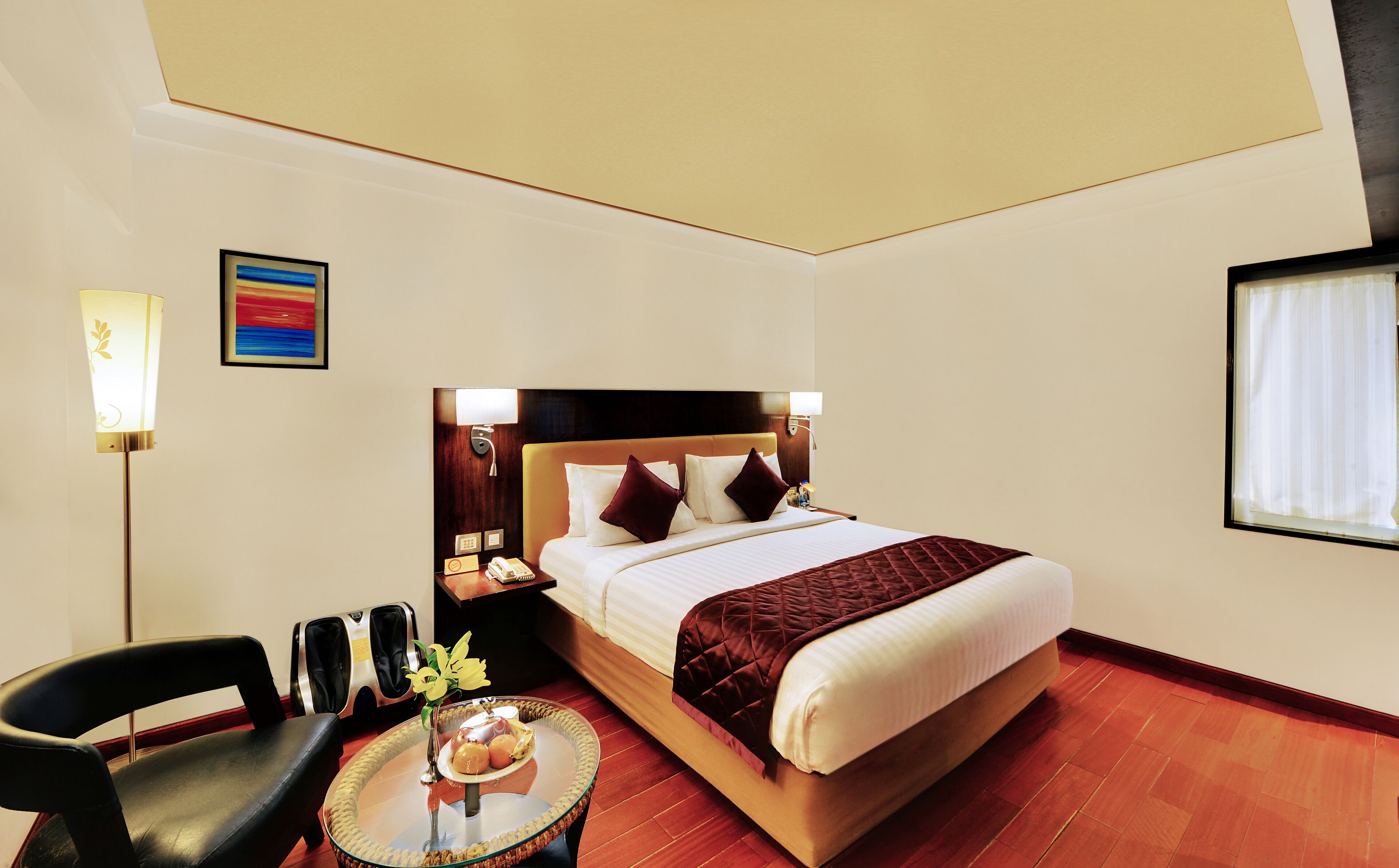 Una habitación de hotel con cama, mesita de noche, silla, lámpara y una pequeña mesa con un jarrón de flores.