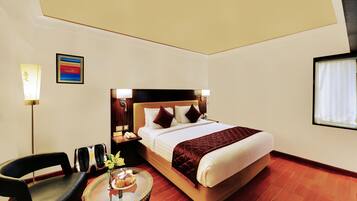 A hotel room with a bed, bedside table, chair, lamp, and a small table with a vase of flowers.