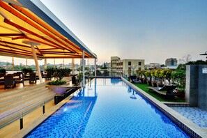 A swimming pool with a sunlit patio area, steps leading to the pool, and potted plants around the pool's edge. - Iris Hotel (Bengaluru)
