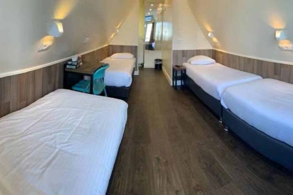 A narrow, well-lit room with two single beds, a small desk, and a chair.