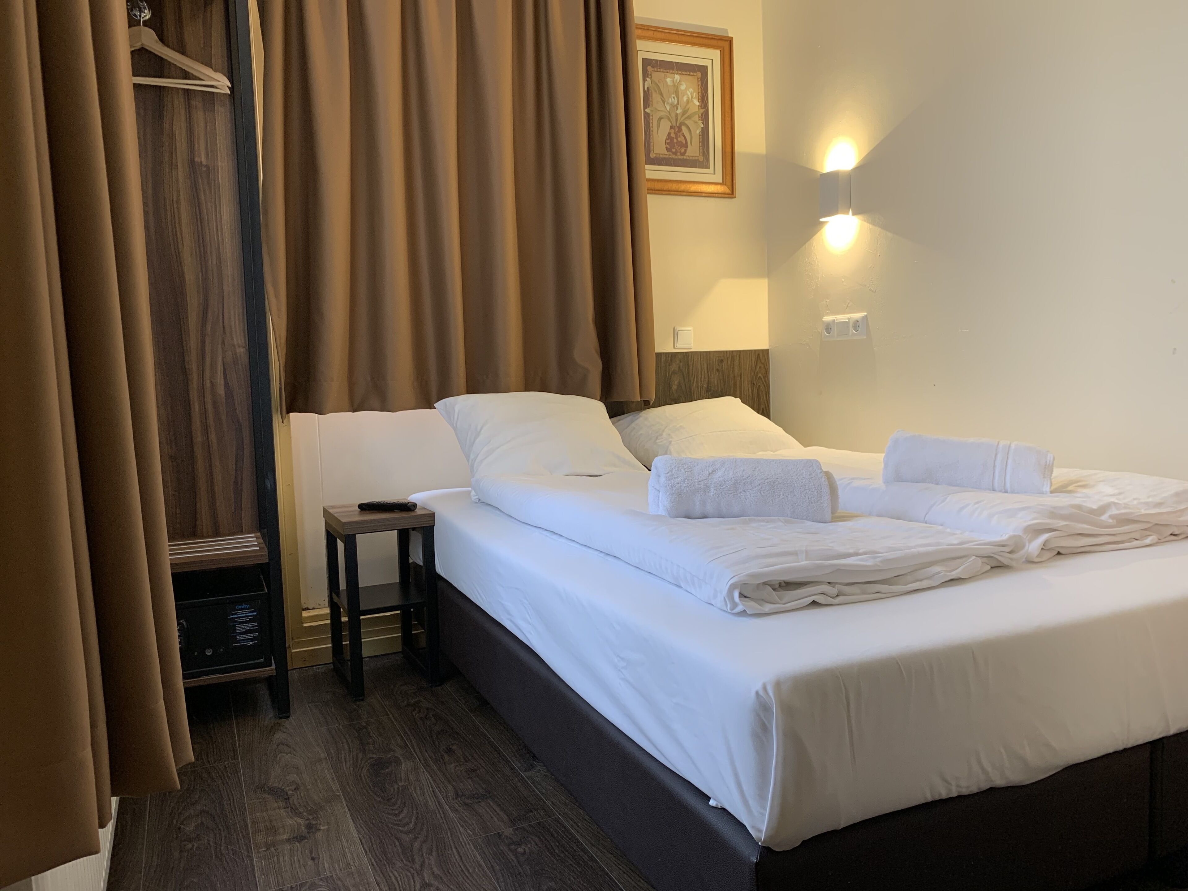 A hotel room with a bed, a bedside table, a lamp, and a picture on the wall.
