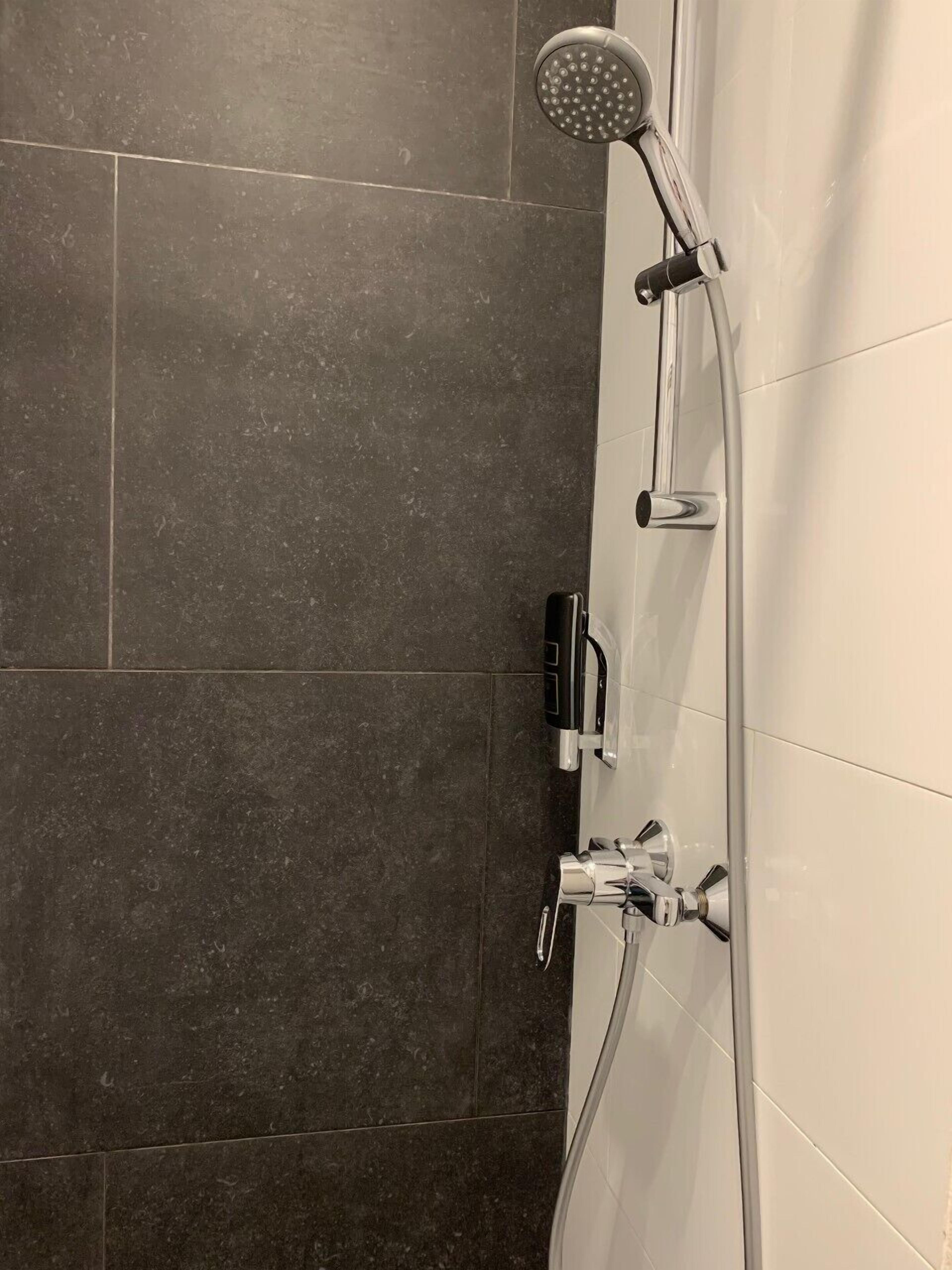 Une douche équipée d’un pommeau de douche à main et d’un panneau de commande fixé au mur.