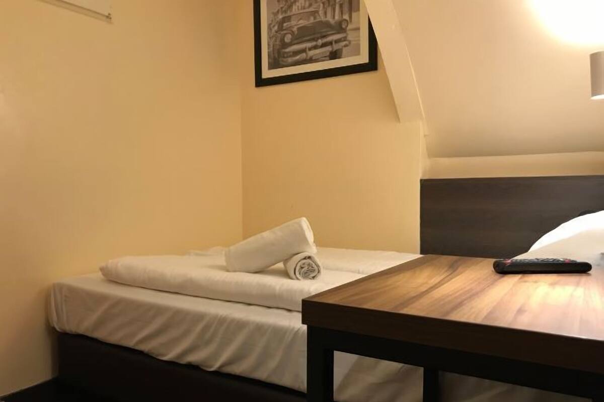 A hotel room with a bed, a small table, and a remote control on the table.
