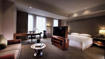 A hotel room with a bed, a TV, a desk, a chair, a coffee table, and a lamp.