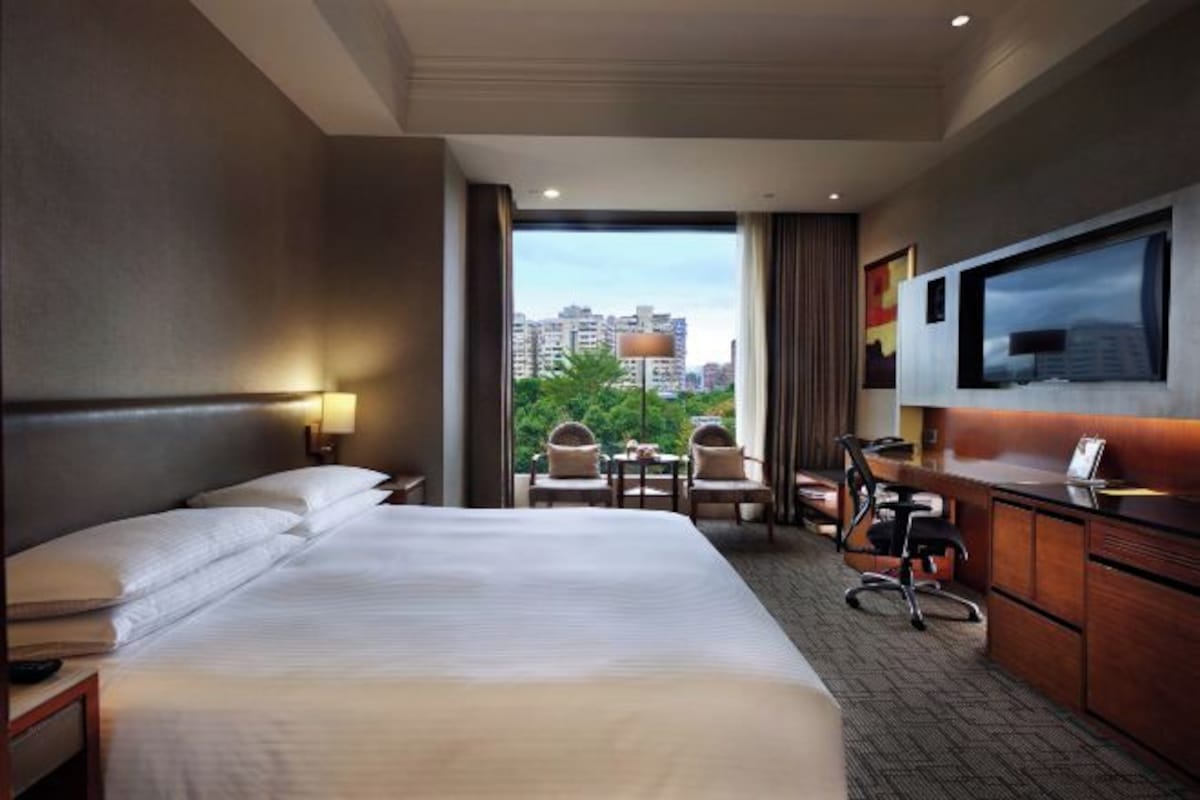 A hotel room with a large bed, a desk, a chair, and a TV on the wall.