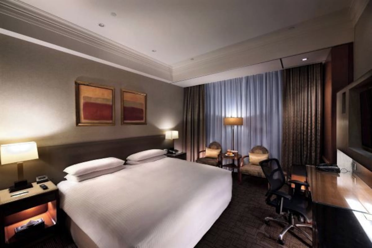 A hotel room with a large bed, bedside tables, a desk, a chair, a television, and a window with curtains.
