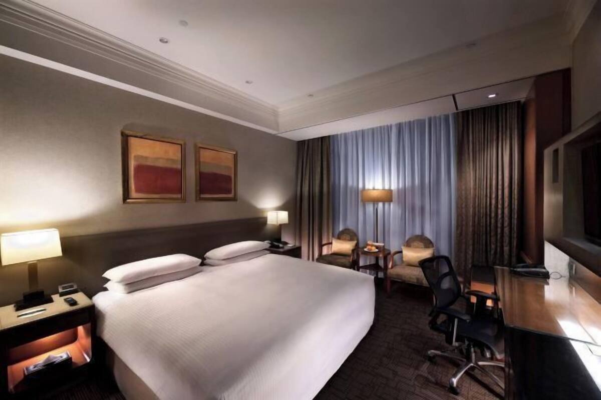 A hotel room with a large bed, bedside tables, a desk, a chair, a television, and a window with curtains.