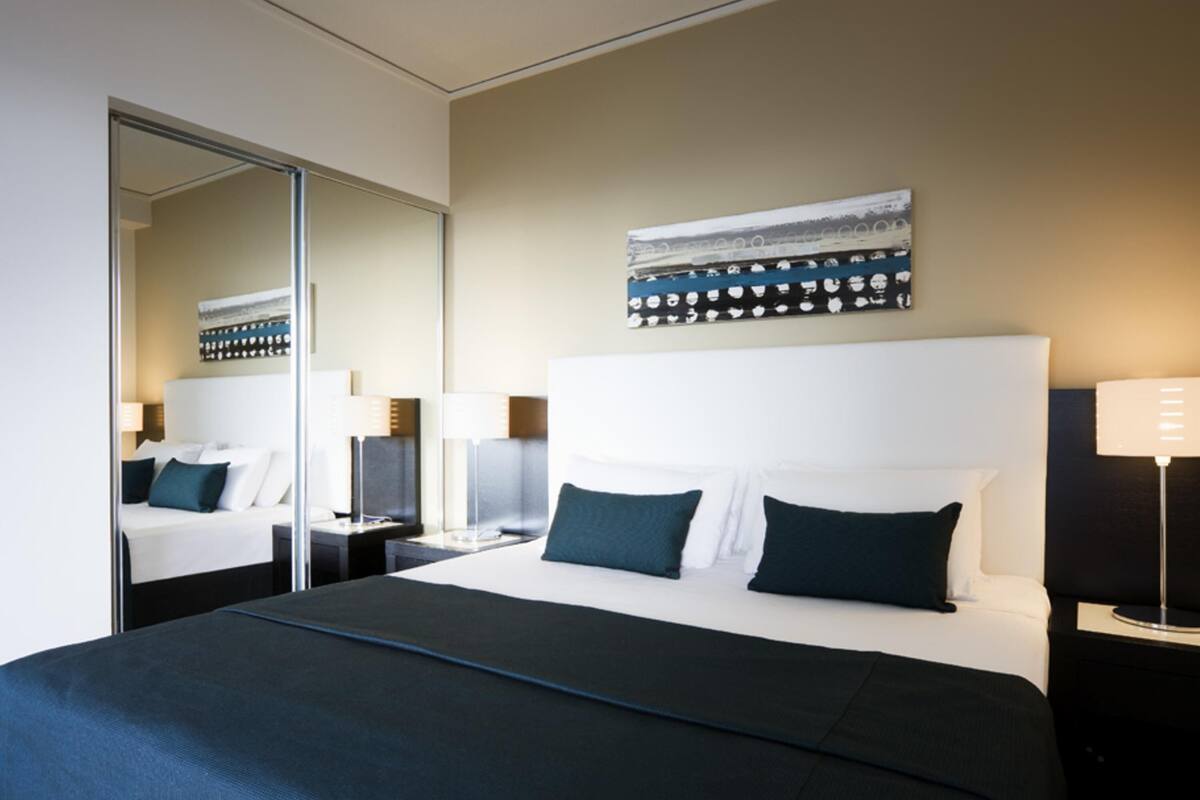 Ein Hotelzimmer mit einem großen Bett, einem Spiegel, einem Bild an der Wand und einem Nachttisch mit einer Lampe.