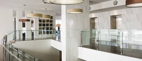 Un'elegante hall d'albergo moderna con ringhiera in vetro, pavimento in marmo e lampade dal design contemporaneo.