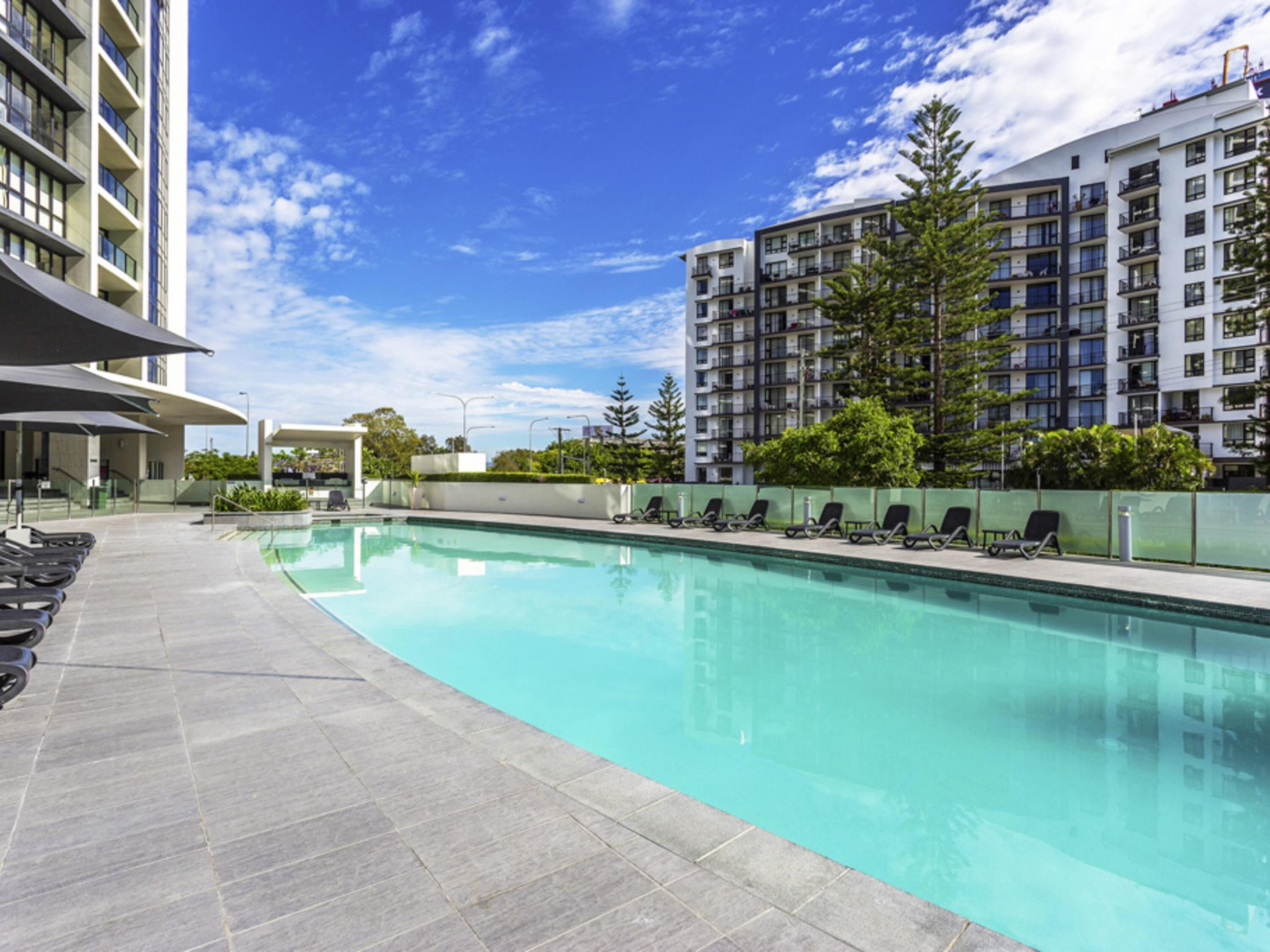 A swimming pool with lounge chairs, surrounded by modern buildings and trees.