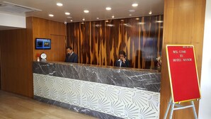 A hotel reception desk with a wooden panel wall, a marble counter, and a red welcome sign. - The Manor Hotel (Chhatrapati Sambhajinagar)