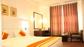 A hotel room with a large bed, a desk, a chair, a mirror, and curtains. - The Manor Hotel (Chhatrapati Sambhajinagar)