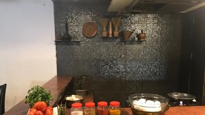 A kitchen counter with various ingredients and utensils, a decorative wall, and a rustic wooden table. - The Manor Hotel (Chhatrapati Sambhajinagar)