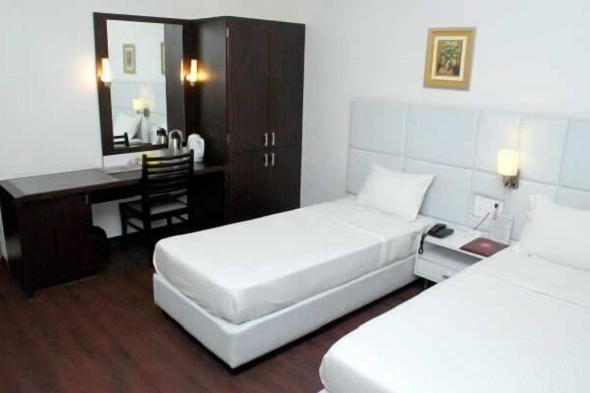 A hotel room with two beds, a desk, a chair, a wardrobe, and a mirror.