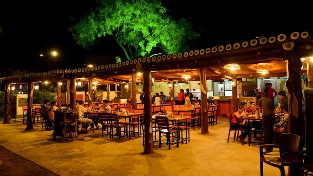 An outdoor restaurant with tables and chairs, a tree, and people dining. - The Manor Hotel (Chhatrapati Sambhajinagar)