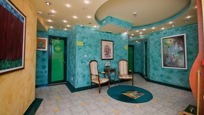 Un hall d’entrée aux murs de couleur turquoise, une porte verte, deux chaises en bois, une petite table et un tapis rond.