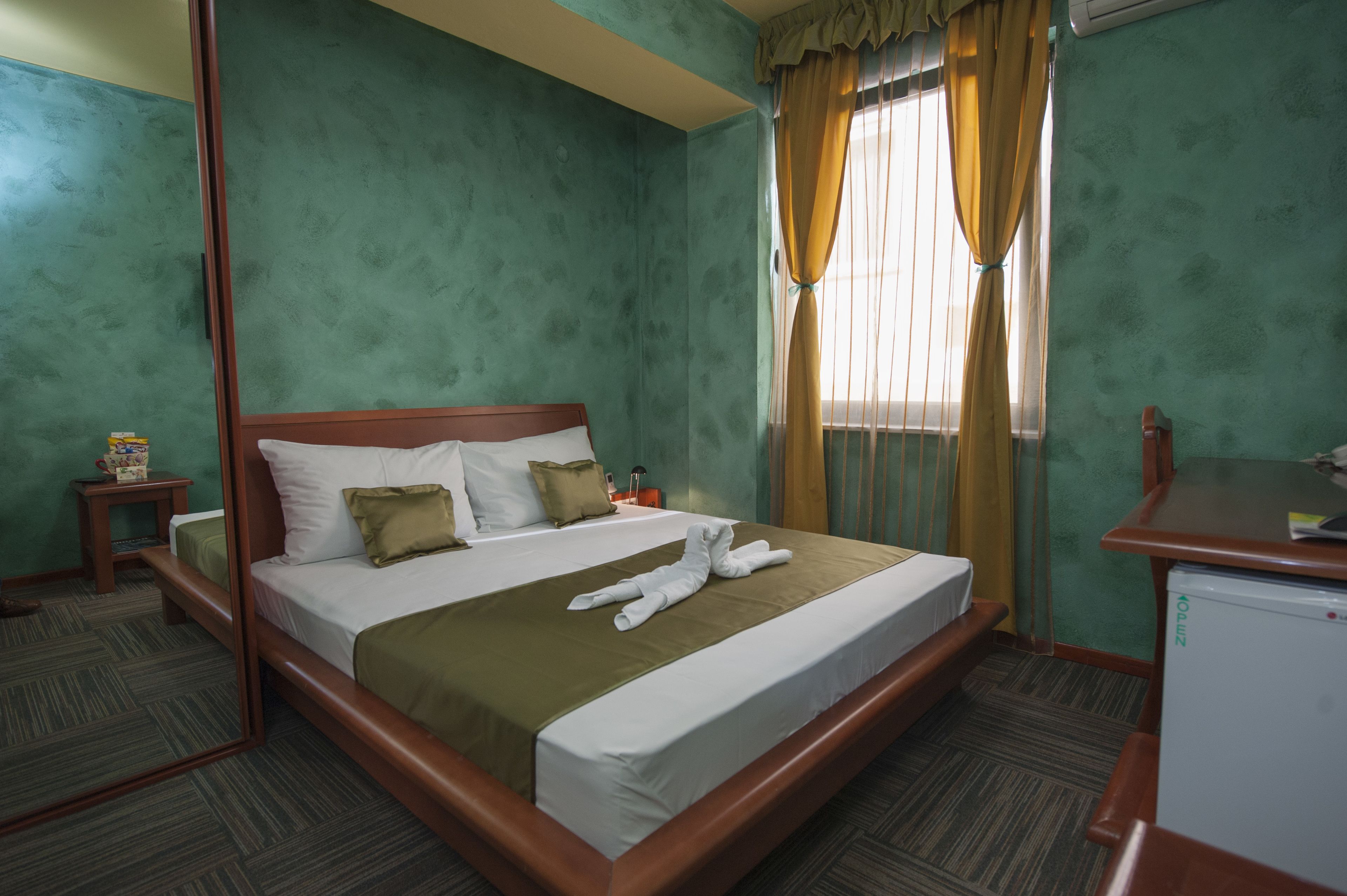 Habitación de hotel con una cama grande, una mesita de noche, un escritorio y una ventana con cortinas.