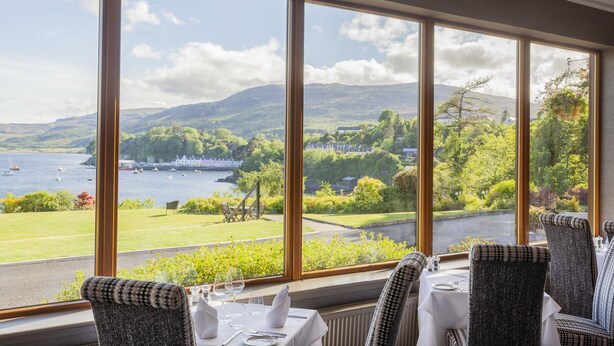 A dining area with large windows overlooking a scenic view of a lake, boats, and greenery. - Cuillin Hills Hotel (Portree)