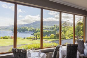 A dining area with large windows overlooking a scenic view of a lake, boats, and greenery.