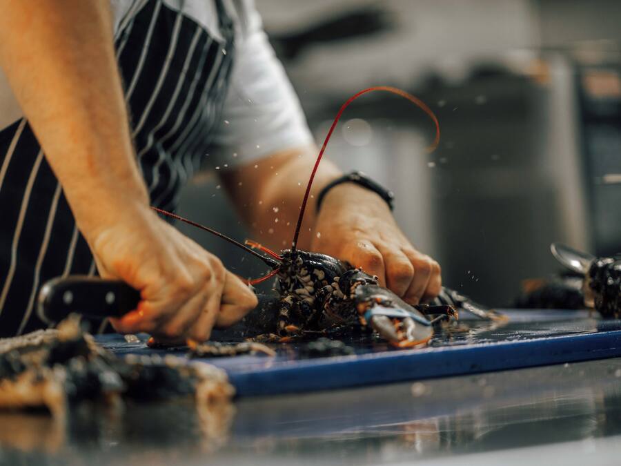 A person preparing food, specifically cutting a lobster on a cutting board.
