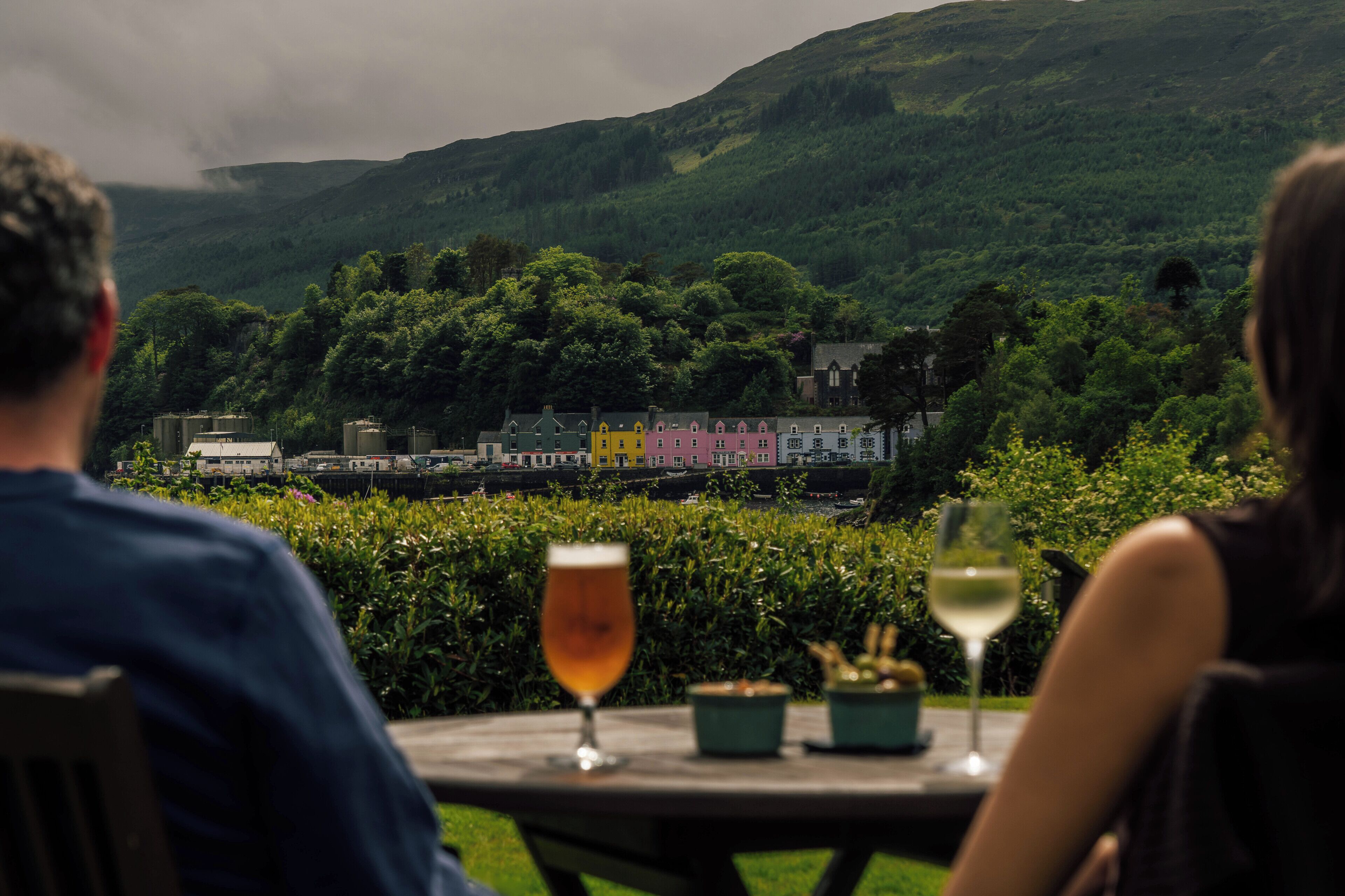 A couple seated at a table with a view of a hillside and colorful buildings in the distance.