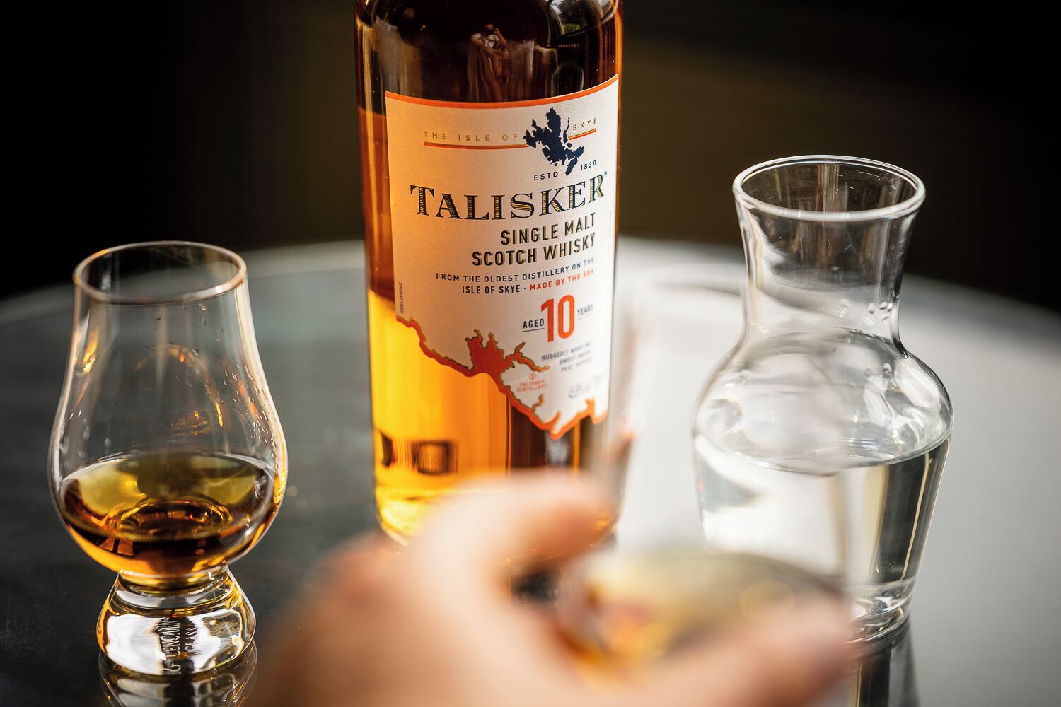 Une bouteille de whisky écossais de malt unique Talisker, un verre de whisky et un pichet en verre transparent sur une table.