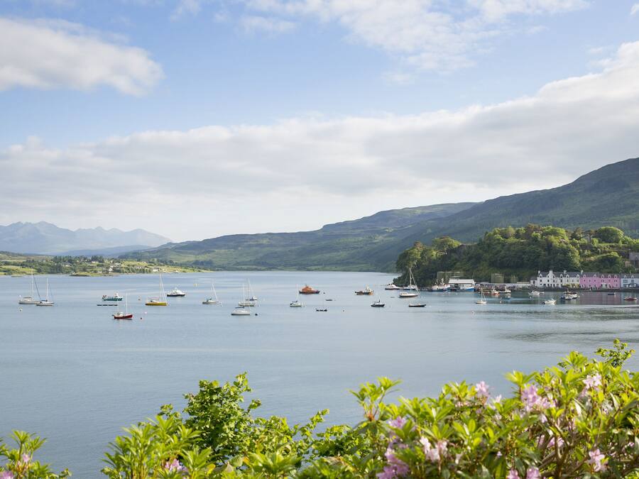A coastal view with boats on a calm sea, a green landscape, and a building with a pink facade.