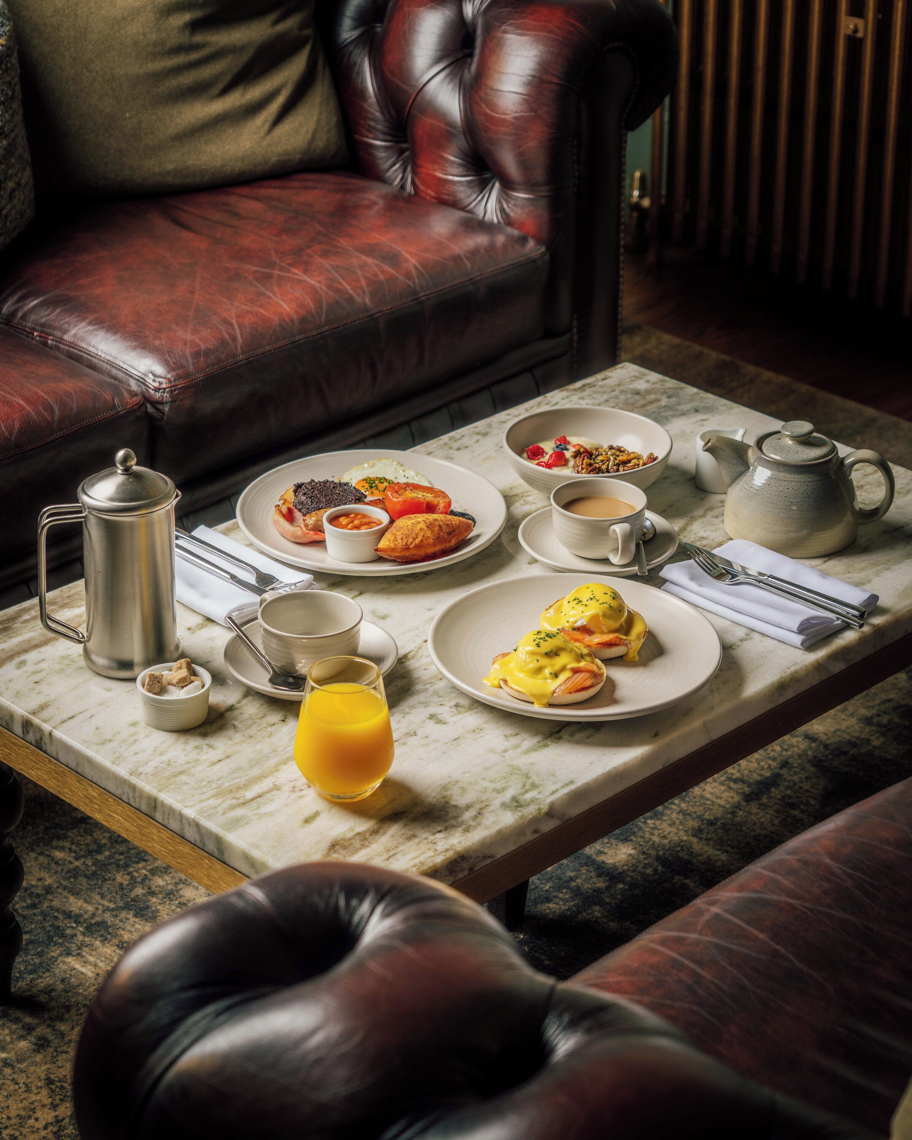 A breakfast setting with a coffee pot, teapot, and plates of food on a marble table.