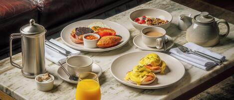 A breakfast setting with a coffee pot, teapot, and plates of food on a marble table.