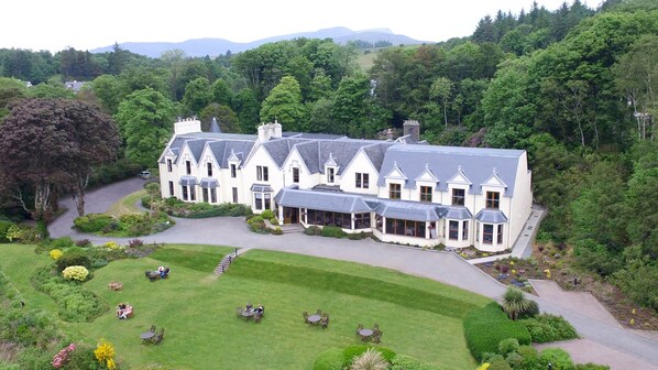 A large, white, multi-story building with a symmetrical design, surrounded by lush greenery and a winding road.