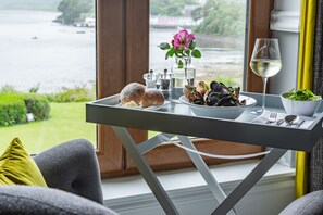 A dining table with a view of a lake, a glass of white wine, mussels, bread, and a flower vase. - Cuillin Hills Hotel (Portree)