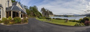 A house with a curved driveway, a lawn, and a view of a lake with boats.