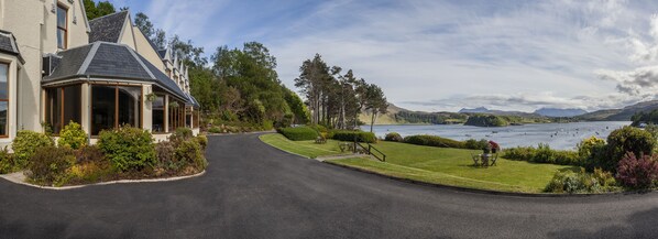 A house with a curved driveway, a lawn, and a view of a lake with boats.