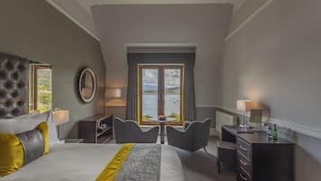 Habitación de hotel con una cama grande, dos sillones, un escritorio y vistas al agua.