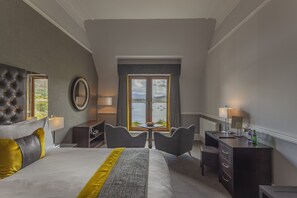 A hotel room with a large bed, two armchairs, a desk, and a view of the water. - Cuillin Hills Hotel (Portree)