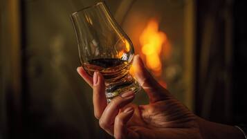 A hand holding a glass with a liquid, set against a blurred background with a warm light source.